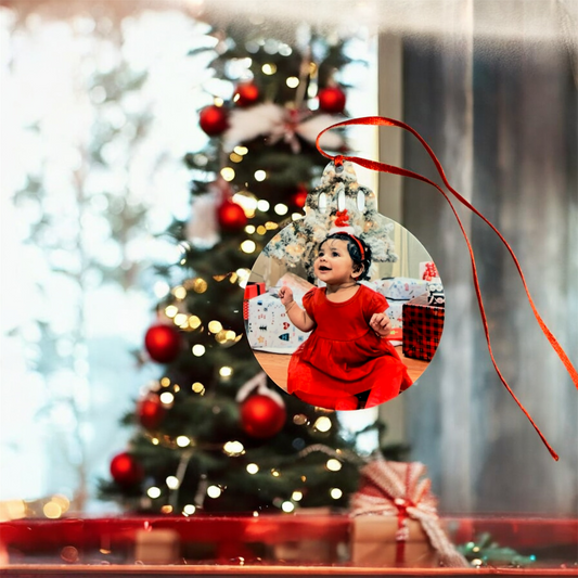 Decorative Christmas ornament with a child in a red dress against a blurred Christmas tree background.
